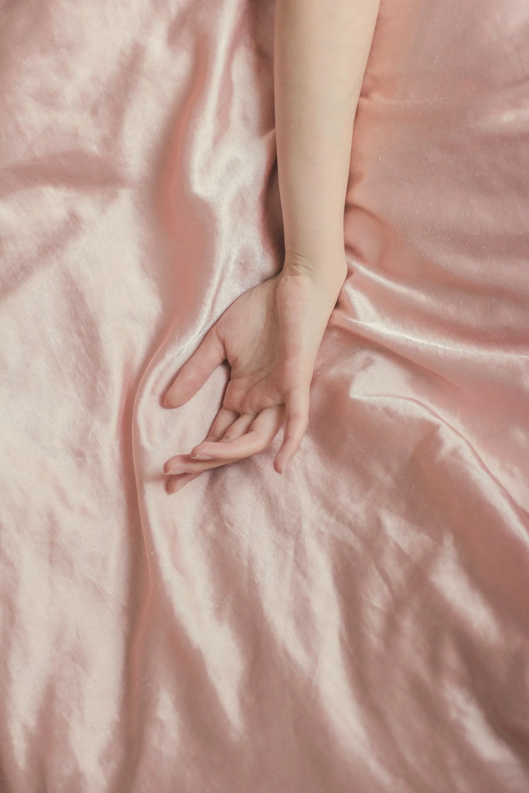 A hand resting on pink silk sheets